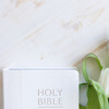 A white holy bible and fresh white tulips laying on a white wood table shot from above with copy space