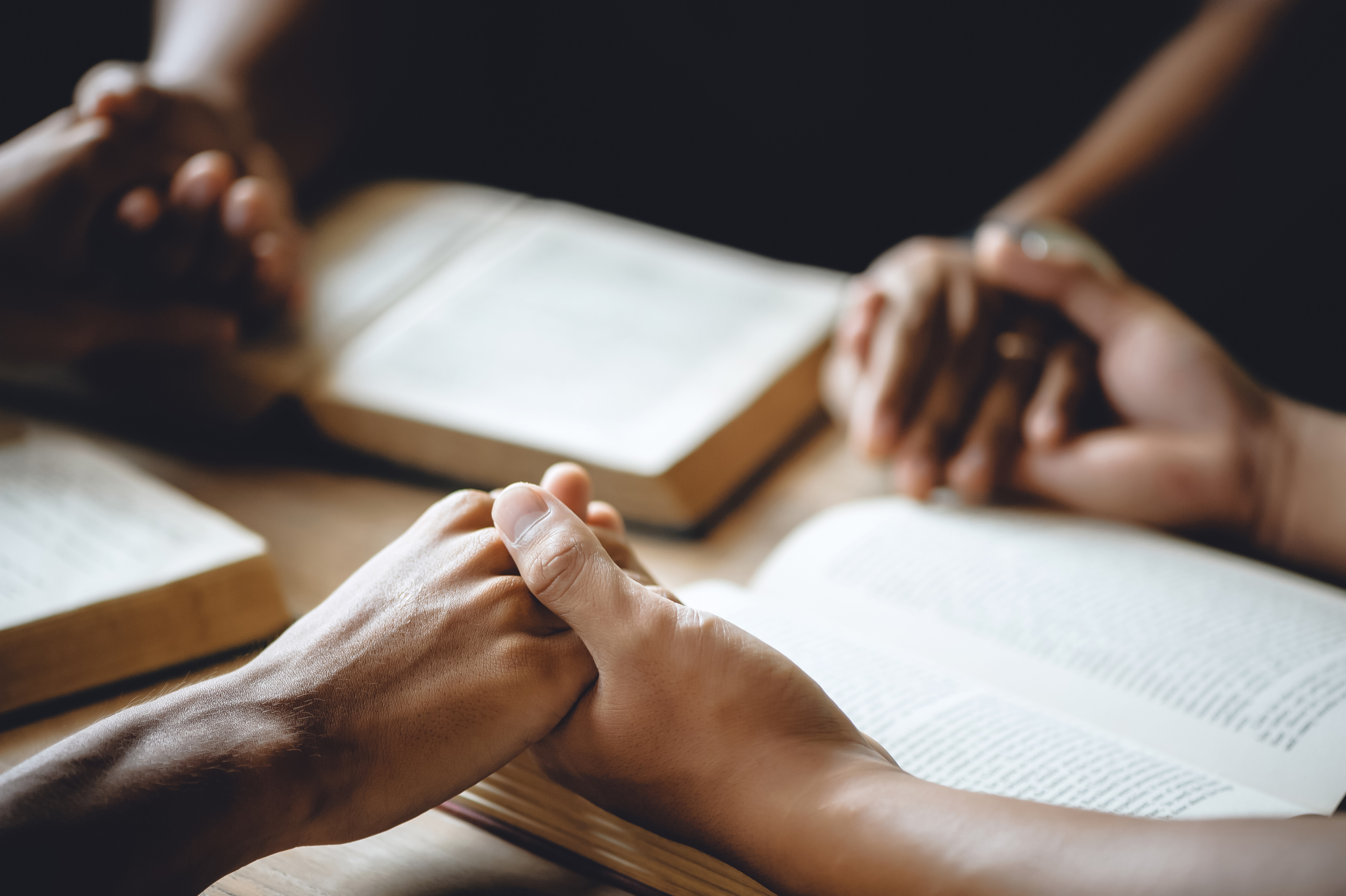 Hands clasped on top of open Bibles on a table