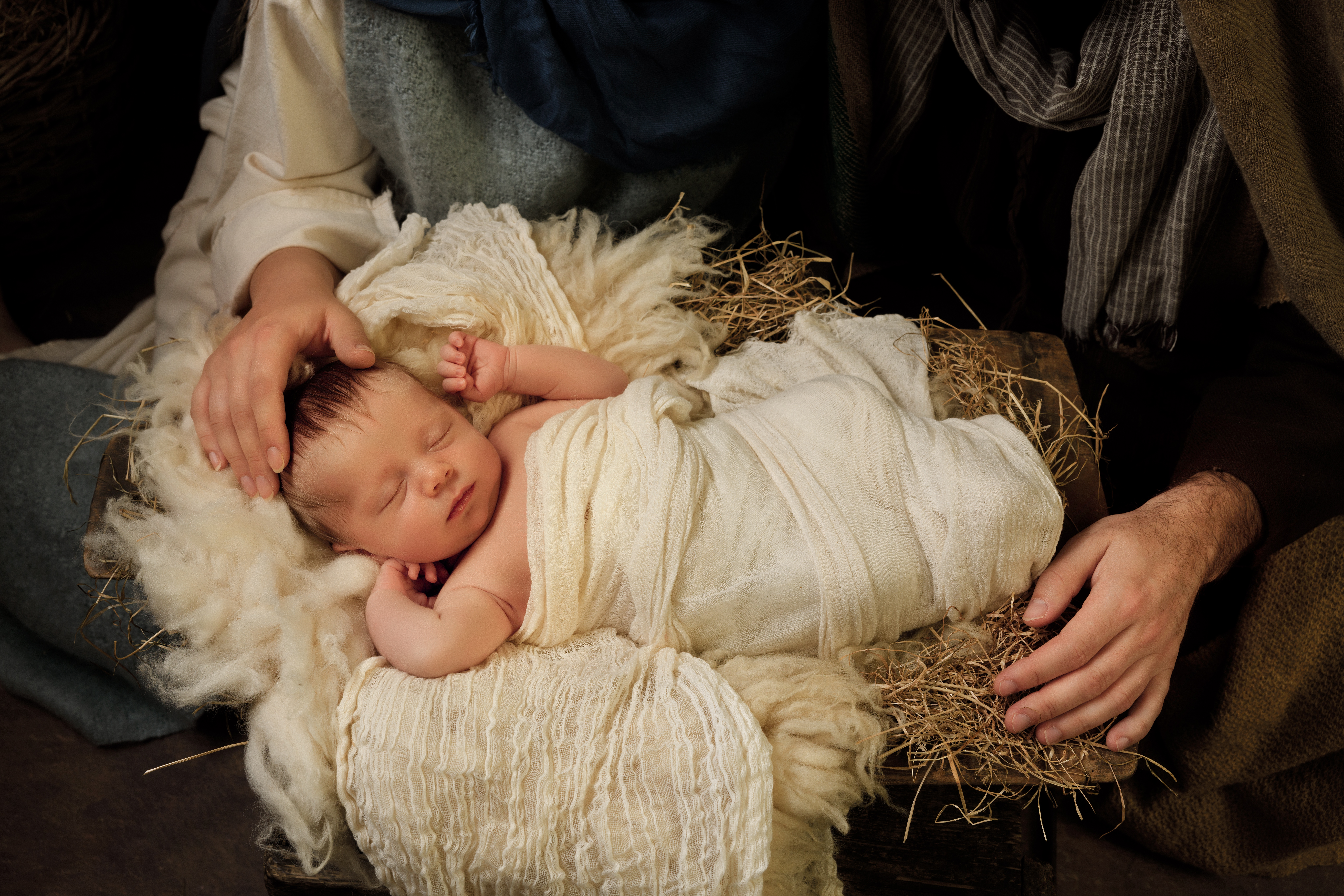 Parents' hands caring for their 9 days old baby boy in an authentic Christmas nativity scene