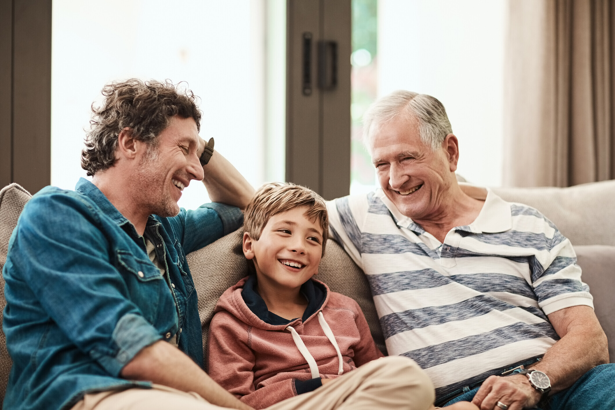 Cropped shot of a cheerful little boy seated on a sofa with his father and grandfather