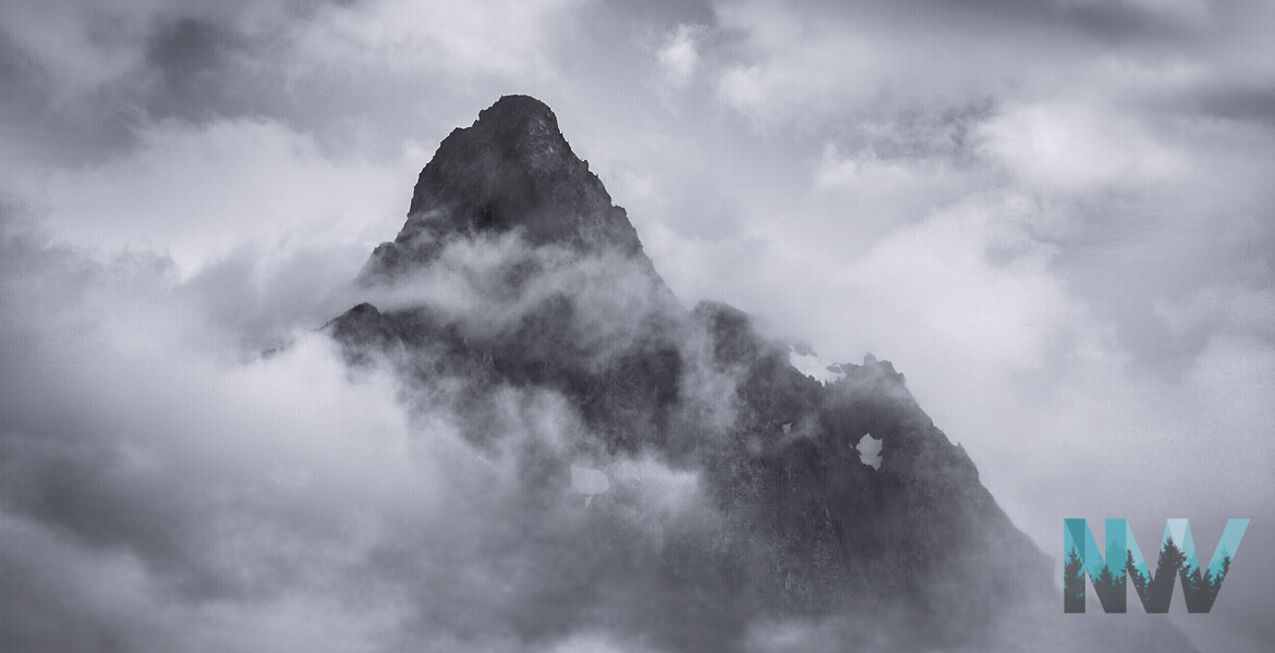 The jagged peak pierces a sea of drifting clouds, revealed and concealed in the same breath.