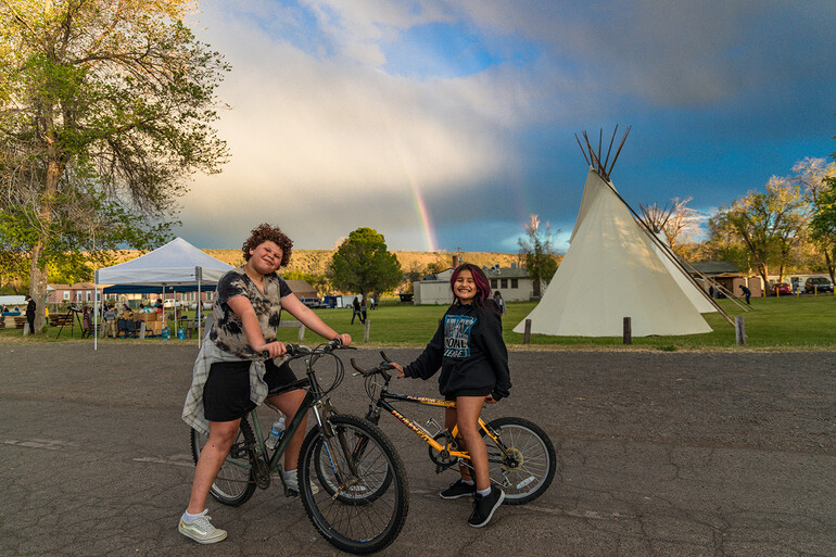 Two girls on bicycles in front of tipis