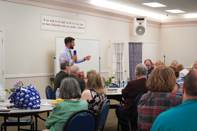 David Lopez speaks into a microphone in front of a whiteboard while a group listens.