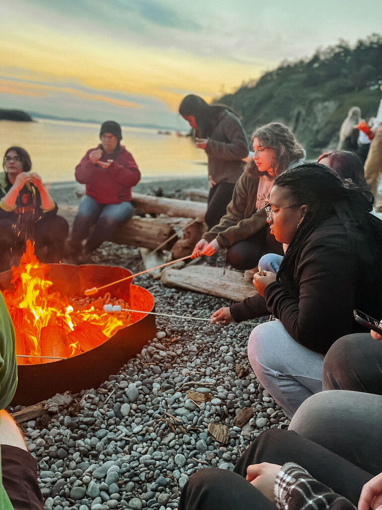 Students gather around a beach-side campfire for sundown worship.