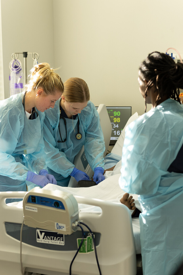 Female nursing students work around hospital bed