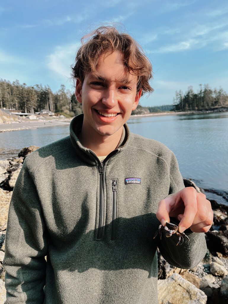 Student holds crab while standing on rocky beach.