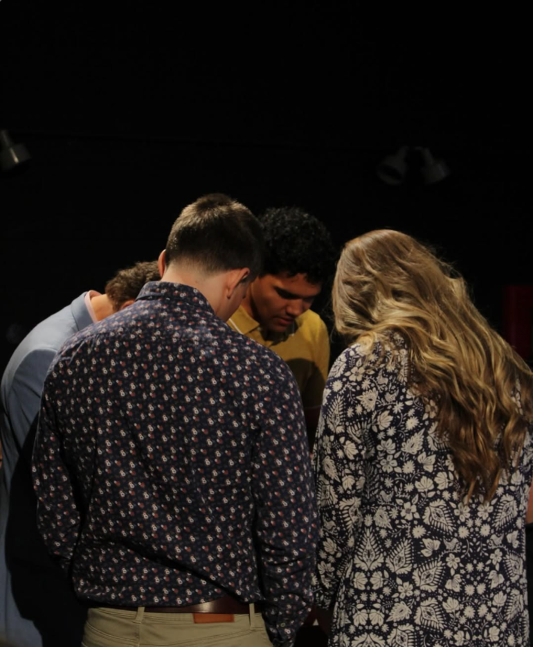 Student pray together in a group, heads bowed.