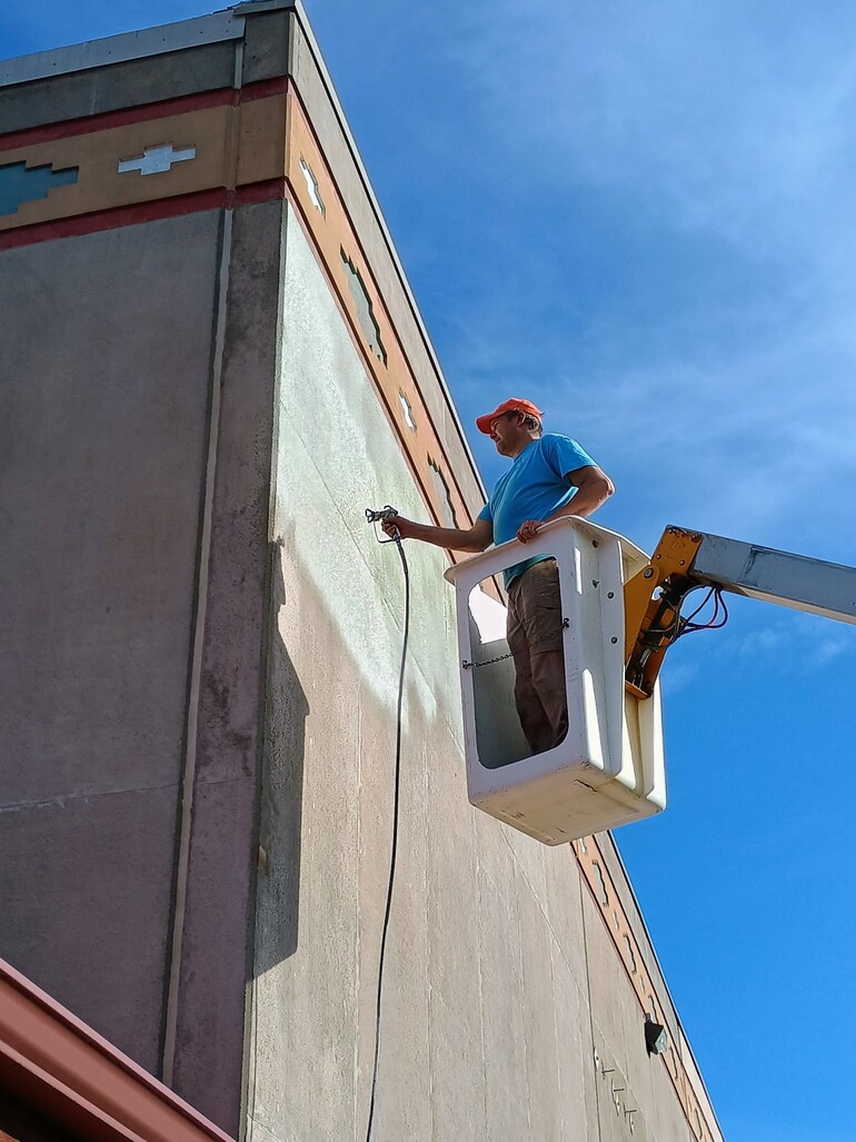 A man on a crane spray paints the outside of a church.