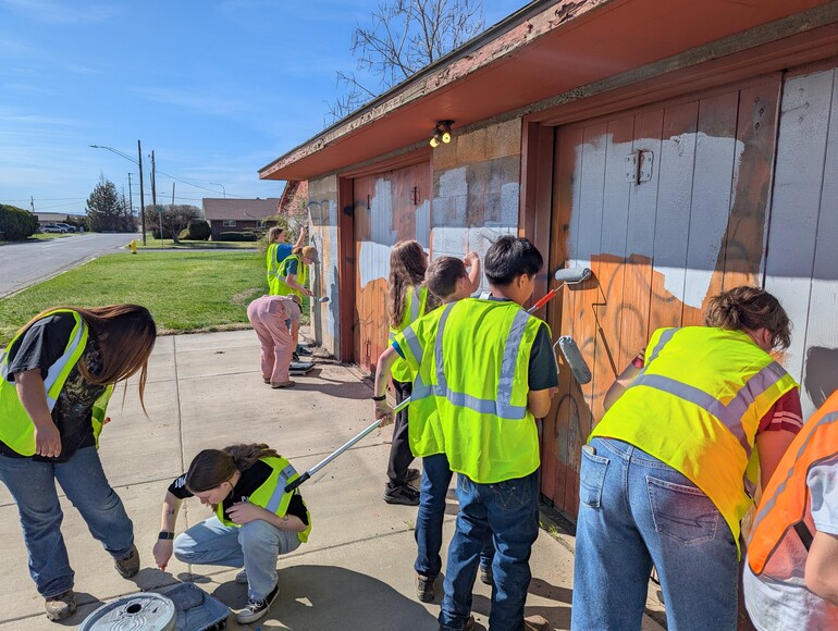 Teens in high visibility vests paint over graffiti covered walls
