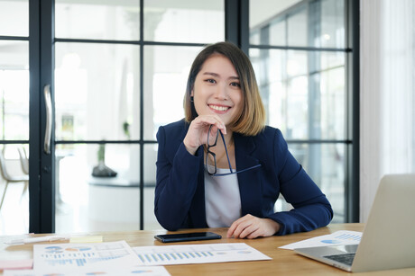 A business woman sits at desk and smiles.