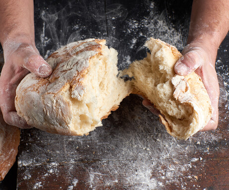 Hands breaking apart a loaf of bread.