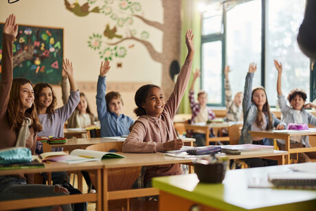 Large group of happy elementary students know the answer in the classroom.