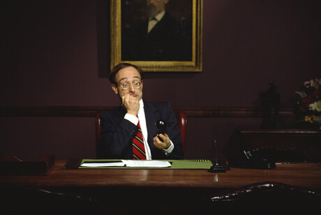 Businessman sits at a desk while holding a phone in shock.