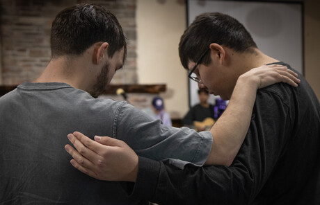 Two young men praying together with arms wrapped around each other.