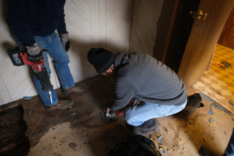 Two volunteers with power tools work to replace old flooring.