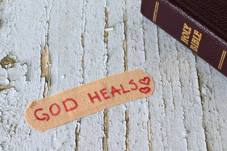 God heals, handwritten text on bandage with closed holy bible book on wooden background. Christian biblical concept of mercy, love, compassion and grace.