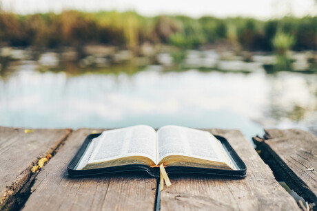 Open Bible on a wooden board near the river.