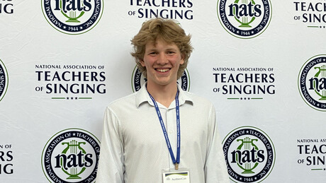 Luke Palau standing in front of a banner at singing competition.