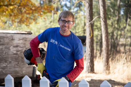 Smiling Volunteer with a Serve One More T-shirt standing in a backyard holding a String Trimmer