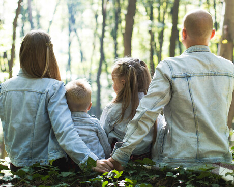 A family of four, husband, wife, son, and daughter, sitting in nature with their back to the camera.