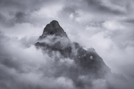 The jagged peak pierces a sea of drifting clouds, revealed and concealed in the same breath.