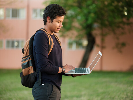 A college student walking outside using a laptop on the go.