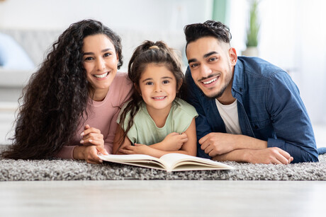 Portrait Of Happy Parents Reading Book With Their Little Daughter