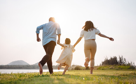 Happy family in the park sunset light. family on weekend running together in the meadow with river Parents hold the child hands.