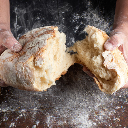 Hands breaking apart a loaf of bread.