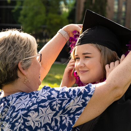 Woman helps female student adjust graduation cap.