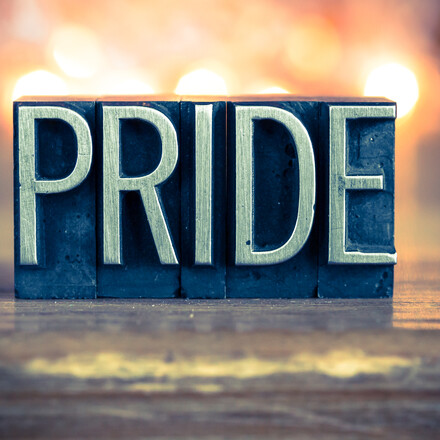 The word PRIDE written in vintage metal letterpress type on a soft backlit background.