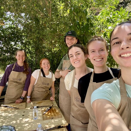 Students wearing aprons gather around outdoor food prep station.