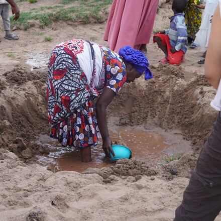 Woman scoops water from muddy puddle