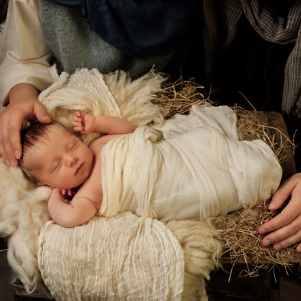 Parents' hands caring for their 9 days old baby boy in an authentic Christmas nativity scene