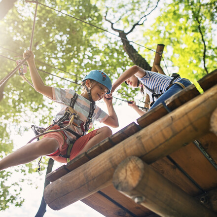 Kids working together on difficult ropes course in adventure park. Sunny summer day.