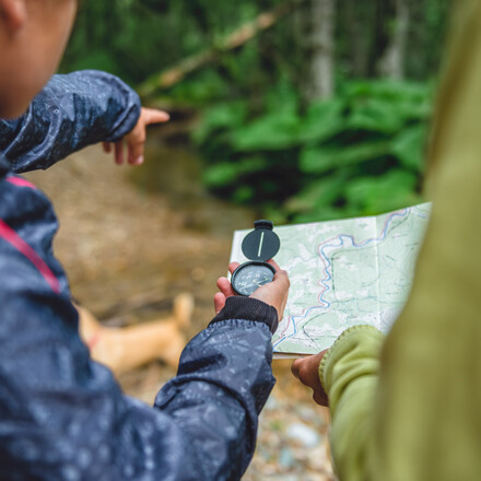 Daughter and mother hiking in forest using compass and map to navigate