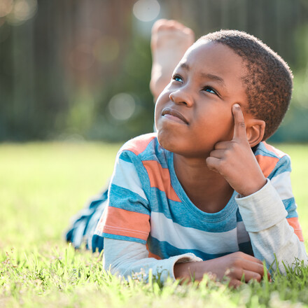 Child on grass looking up and thinking