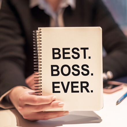 Business woman holds a notebook with the text BEST. BOSS. EVER.