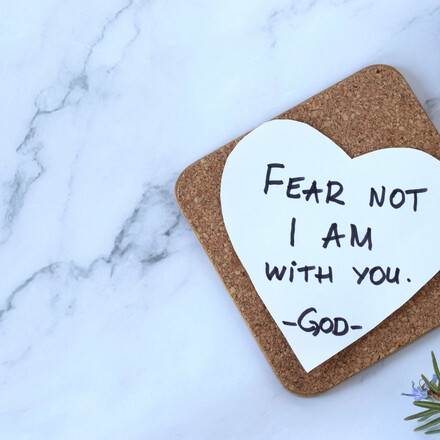 Fear not, I am with you, handwritten verse on heart-shaped note and closed holy bible book. Top table view. Copy space. Words of encouragement and hope from God Jesus Christ, Isaiah 41:10.