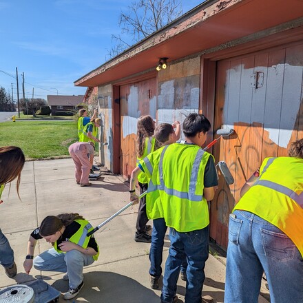 Teens in high visibility vests paint over graffiti covered walls