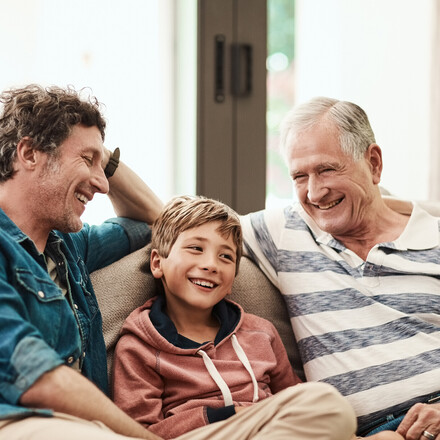Cropped shot of a cheerful little boy seated on a sofa with his father and grandfather