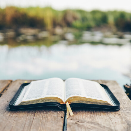 Open Bible on a wooden board near the river.