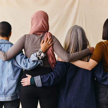 Rear view of four women with arms around each other in support of International Women's Day