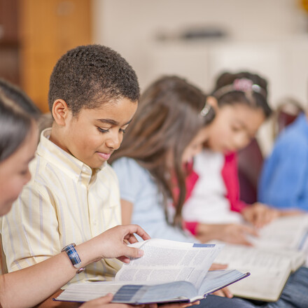 A multi-ethnic group of elementary age children are sitting together and are reading the Bible.