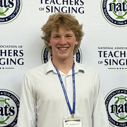 Luke Palau standing in front of a banner at singing competition.
