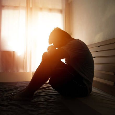 desperate man in silhouette sitting on the bed with hands on head