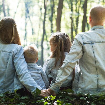 A family of four, husband, wife, son, and daughter, sitting in nature with their back to the camera.
