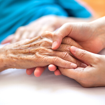 Woman holding senior woman's hand on bed
