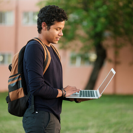 A college student walking outside using a laptop on the go.