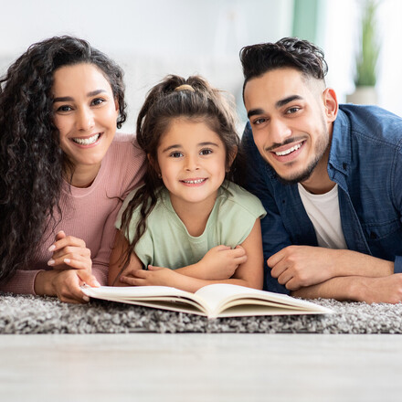 Portrait Of Happy Parents Reading Book With Their Little Daughter